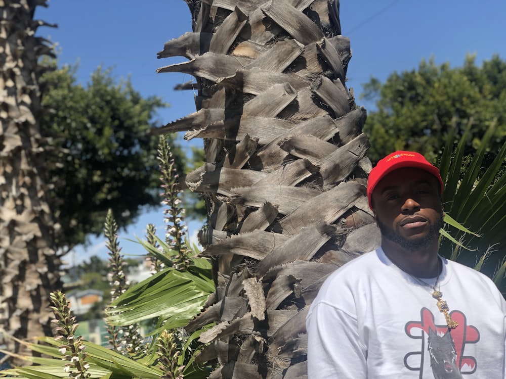 man standing beside tree wearing white crew-neck T-shirt