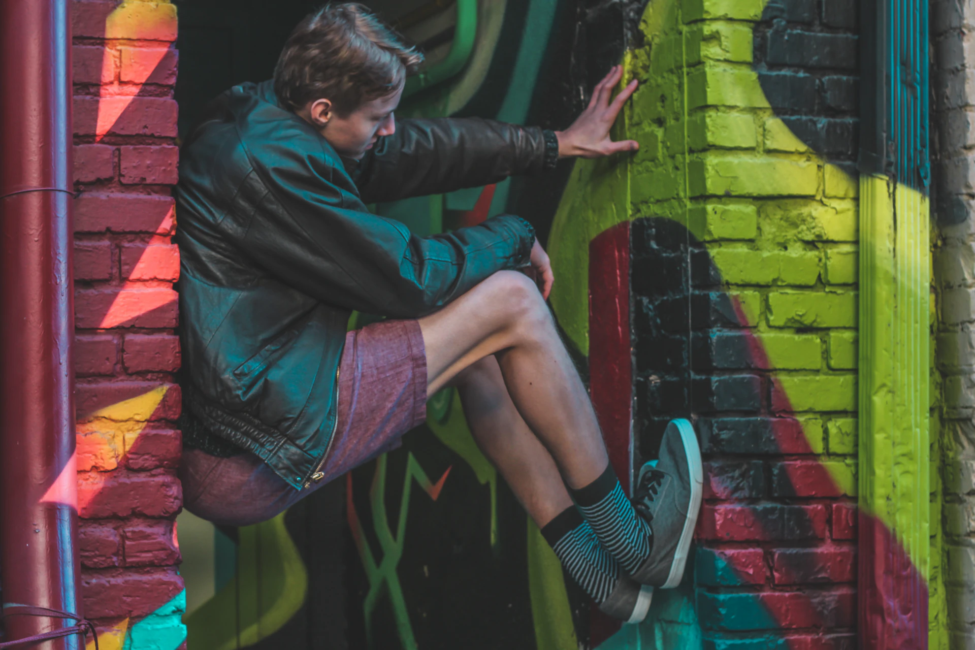 A dynamic shot of a young person mid-motion, rocking a layered outfit with a leather jacket and graphic tee, framed by colorful street art.