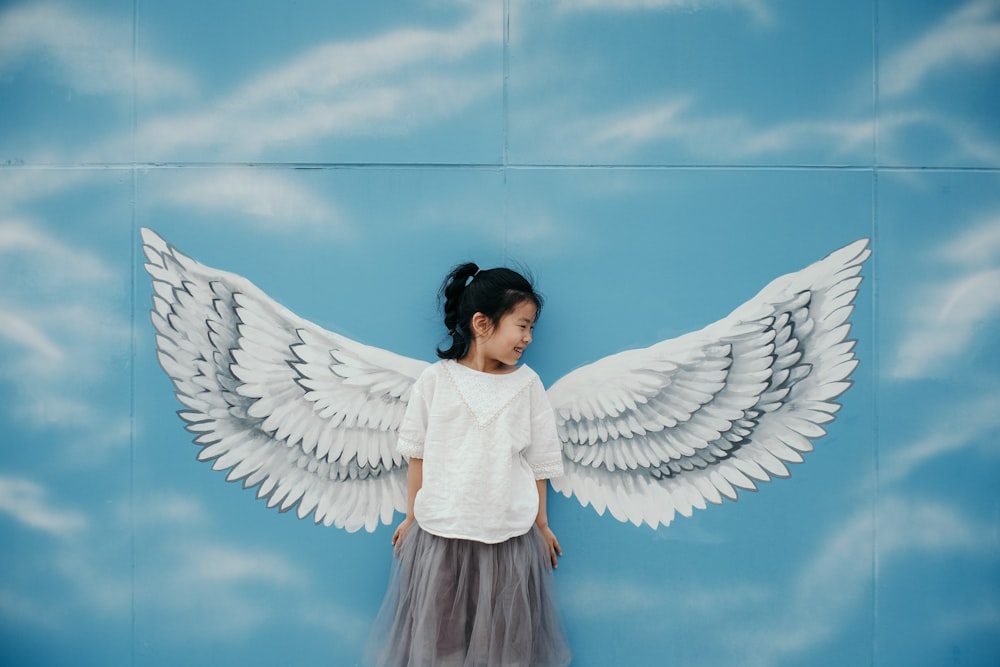 girl leaning on wall with wings mural painting