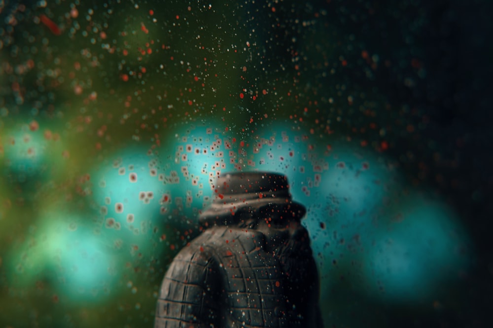 a black vase sitting on top of a window covered in rain