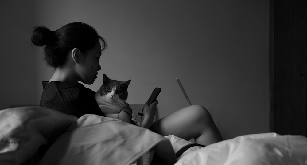 woman holding cat while using smartphone on bed