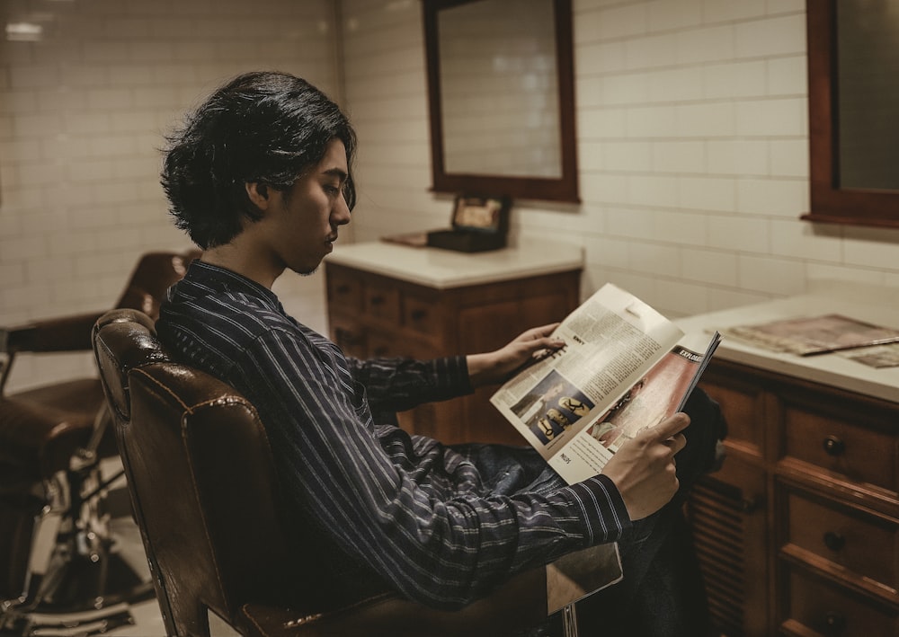 Junge liest Buch, während er auf einem Sofasessel sitzt