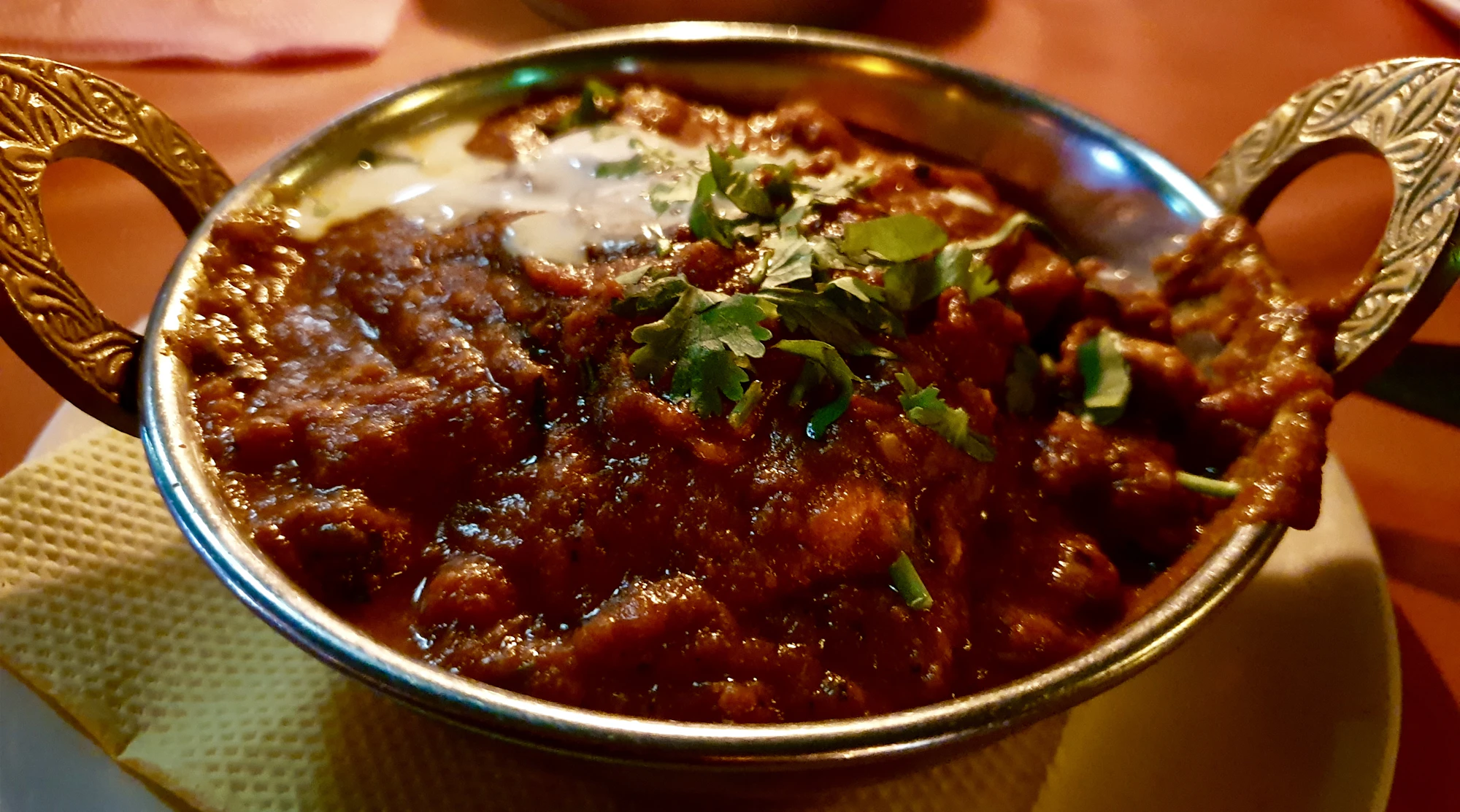 A deep red curry in a hammered copper bowl, finished with coriander