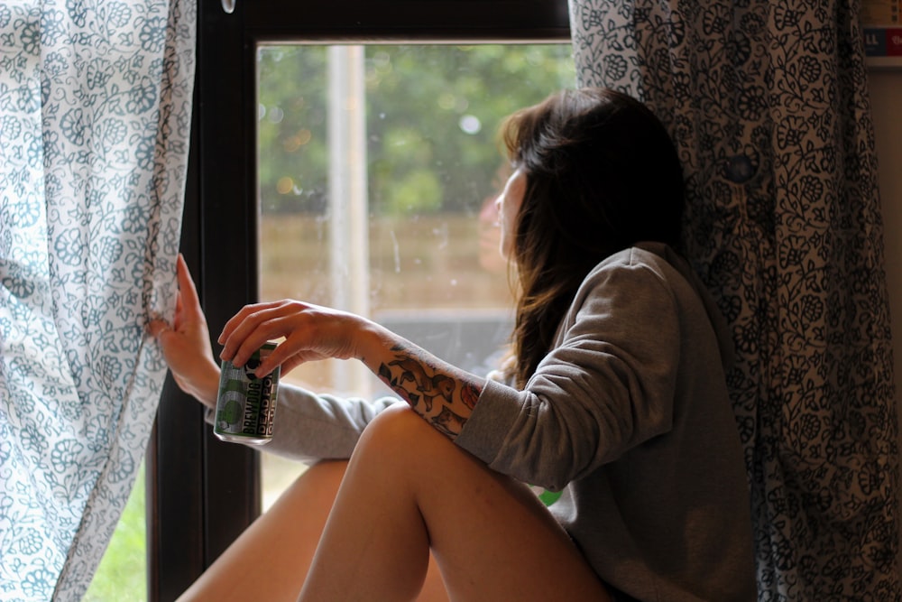 shallow focus photo of woman in gray long-sleeved shirt beside window