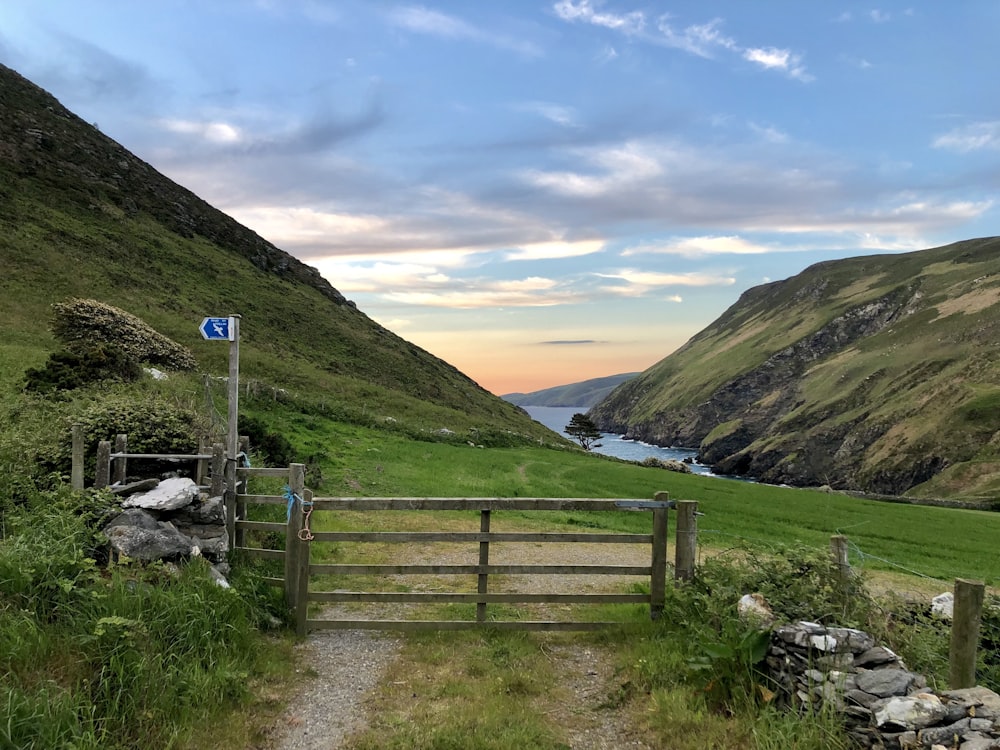 closed gray wooden mini gate near green open field viewing lake and mountain under blue and gray skies