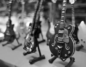 A collection of miniature electric guitars is displayed on stands, with a focus on a black guitar in the foreground. The background is blurred, highlighting varying guitar designs and colors.