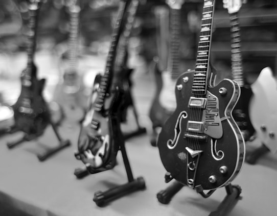 A collection of miniature electric guitars is displayed on stands, with a focus on a black guitar in the foreground. The background is blurred, highlighting varying guitar designs and colors.