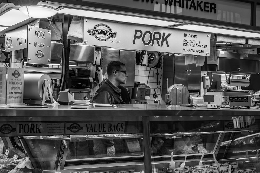 Fotografía en escala de grises de un hombre dentro del mostrador de comida de cerdo
