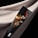 A bouquet of dried flowers wrapped in a sleek black paper against a black and beige fabric backdrop. The arrangement features various textures and colors, including deep reds, soft beiges, and dark browns.