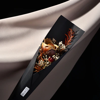 A stylish bouquet wrapped in black paper with a gold ribbon, placed on a white marble surface.