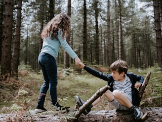 boy and girl playing on three tree log