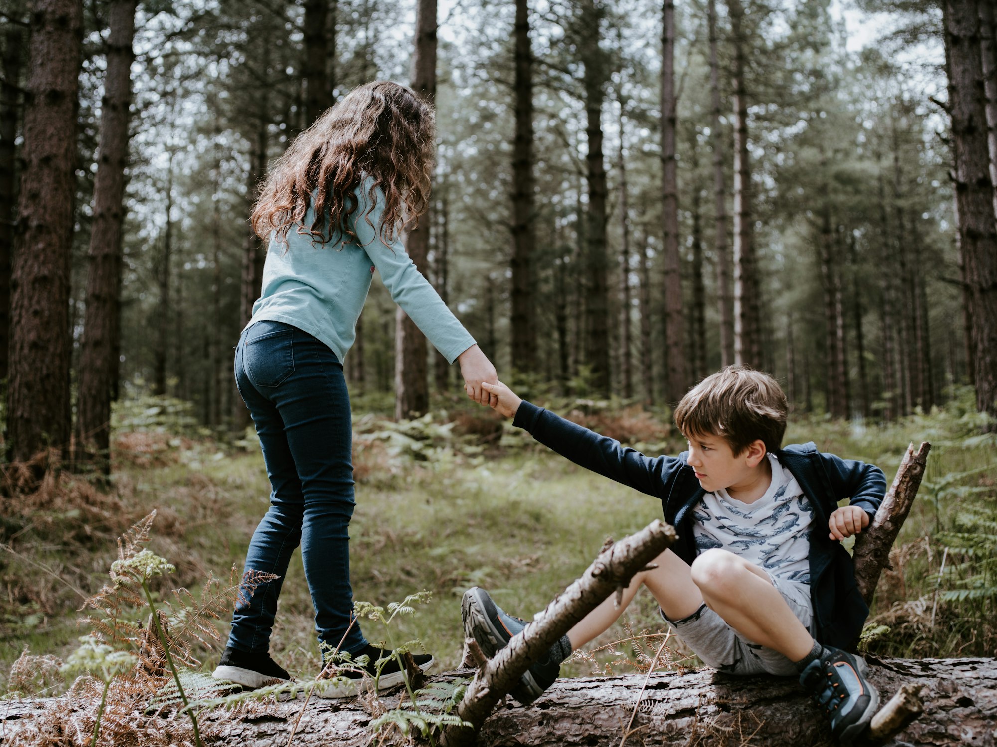 Girl lends hand to help a boy stand up on top of a log.