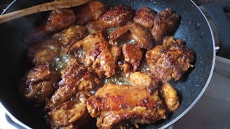 A pan filled with golden-brown, fried chicken pieces. The chicken is sizzling, and there is a wooden spatula resting on the side of the pan.