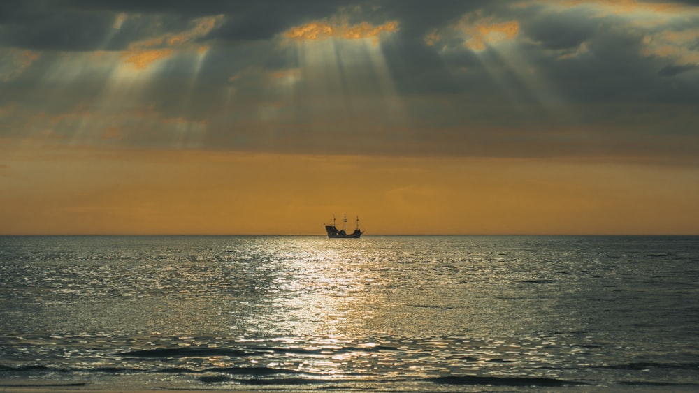silhouette of boat sailing on sea during golden hour