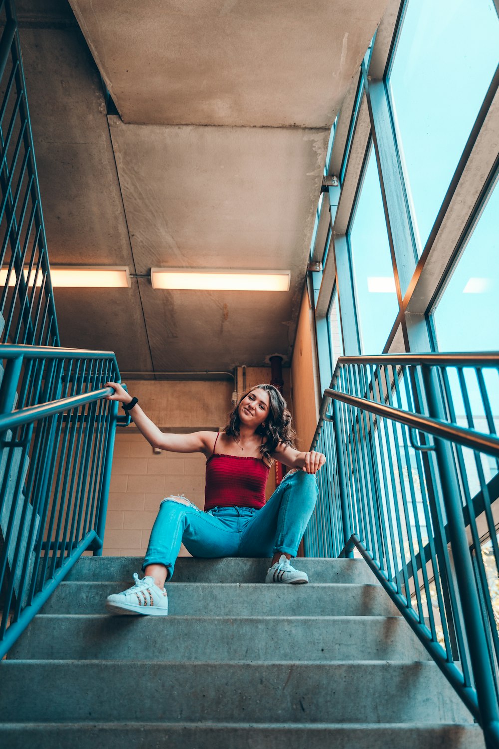 woman in red tank top and blue distressed denim jeans sitting on top of stairs