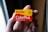 A hand holds a box of Kodak ColorPlus film, displaying the brand name prominently in red and yellow colors. The packaging features details such as 36 exposures and ISO 200. The background is softly blurred, drawing focus to the film box.
