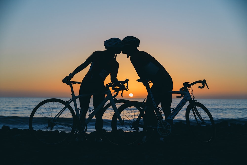 silhouette photography of two people on standing seashore near bikes
