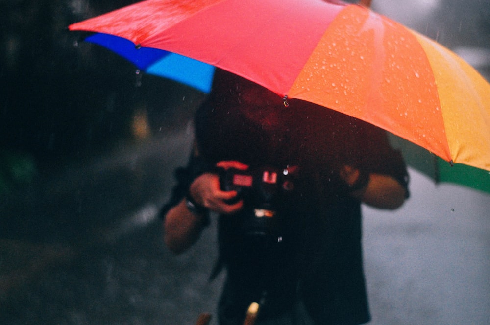 man with camera and multicolored umbrella standing under rain