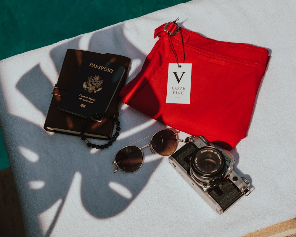 Quatre passeports, des lunettes de soleil, un appareil photo et un pantalon rouge sur un tissu blanc