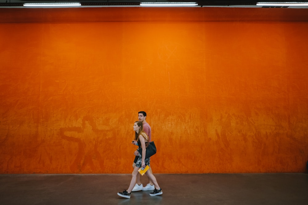woman and man walking beside orange wall