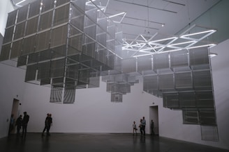 A serene installation featuring suspended geometric forms casting delicate shadows on a white gallery floor.
