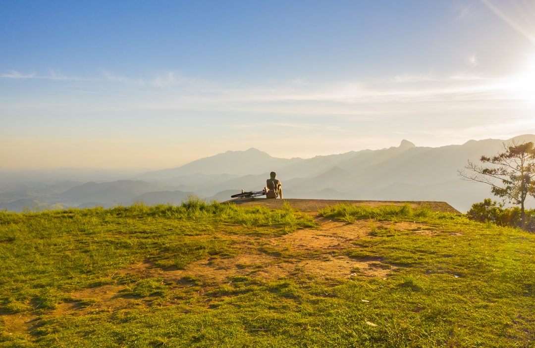 person sitting on cliff overlooking mountain during daytime