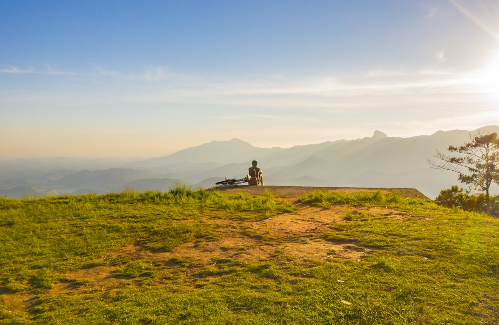 person sitting on cliff overlooking mountain during daytime