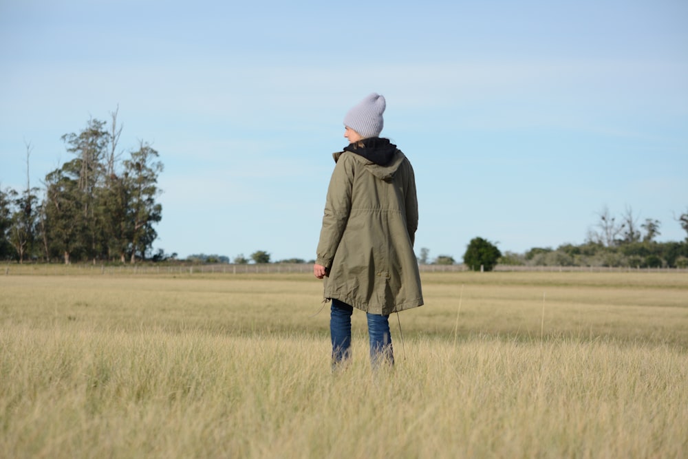 person in green jacket and blue pants standing on grass field during daytime