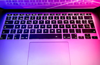 Close-up of hands typing on a laptop keyboard with vibrant purple backlighting.