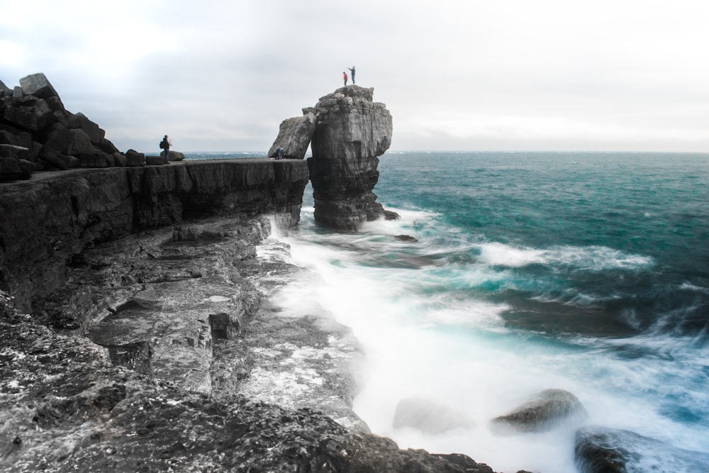 man standing in ledge on top of cliff in beach