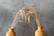 Two ornately decorated ceramic vases are positioned side by side against a textured gray background. Each vase holds golden stalks of wheat that curve gracefully, creating an arch above the vases. The pottery features artistic designs etched into its surface, adding to the rustic and natural aesthetic.