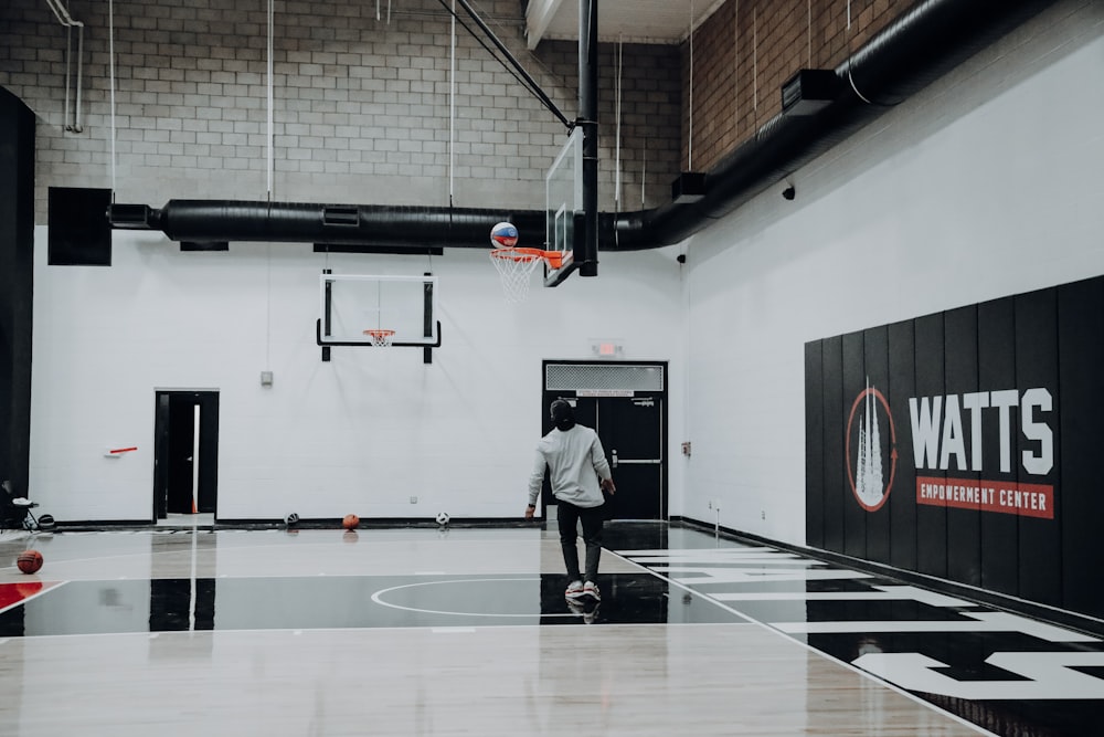 hombre de pie dentro de la cancha de baloncesto mirando la pelota en el aro de baloncesto