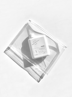 A white plastic bottle labeled 'TONIK' lies on a clear, resealable plastic bag placed on a white background. The light creates distinct shadows, adding a minimalist aesthetic to the scene.