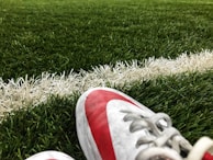 A close-up view of a soccer field, focusing on a pair of red and white cleats resting on the green turf near a white boundary line.