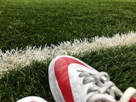 A close-up view of a soccer field, focusing on a pair of red and white cleats resting on the green turf near a white boundary line.