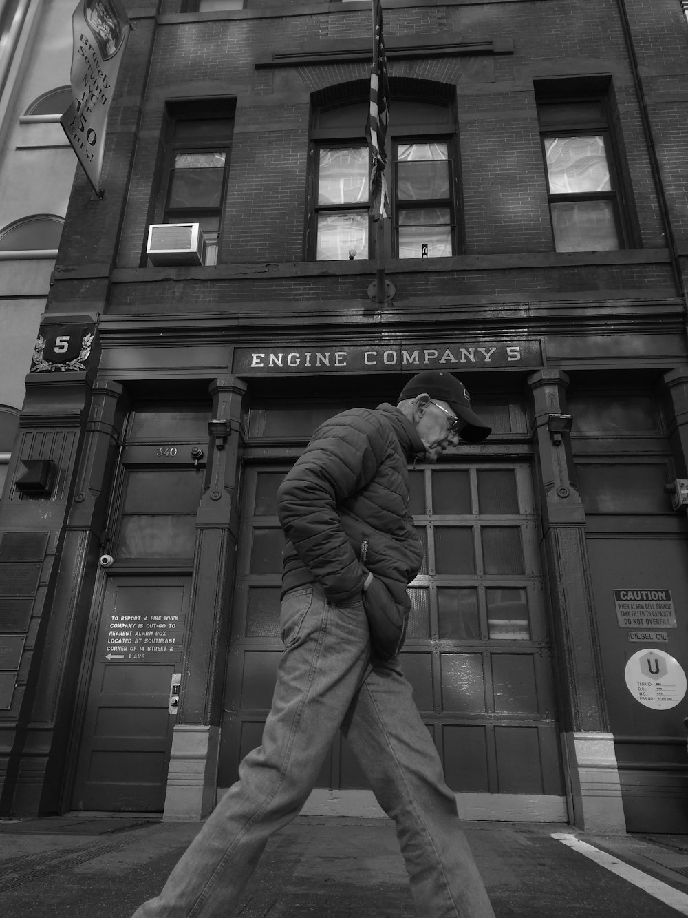Graustufenfoto eines Mannes, der in der Nähe des Gebäudes der Engine Company spazieren geht