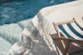 Man testing pool water with a kit beside a shimmering blue pool surrounded by palm trees.