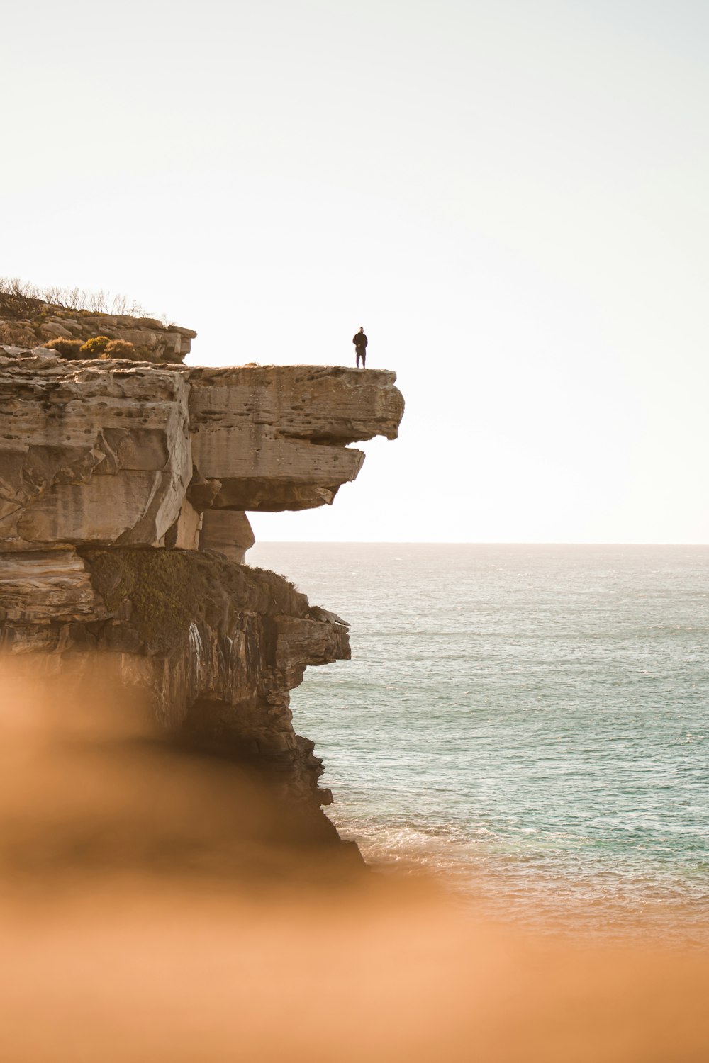 Persona de pie en un acantilado rocoso cerca del cuerpo de agua durante el día