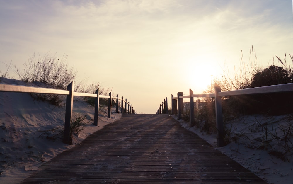 a wooden walkway leading to a beach at sunset