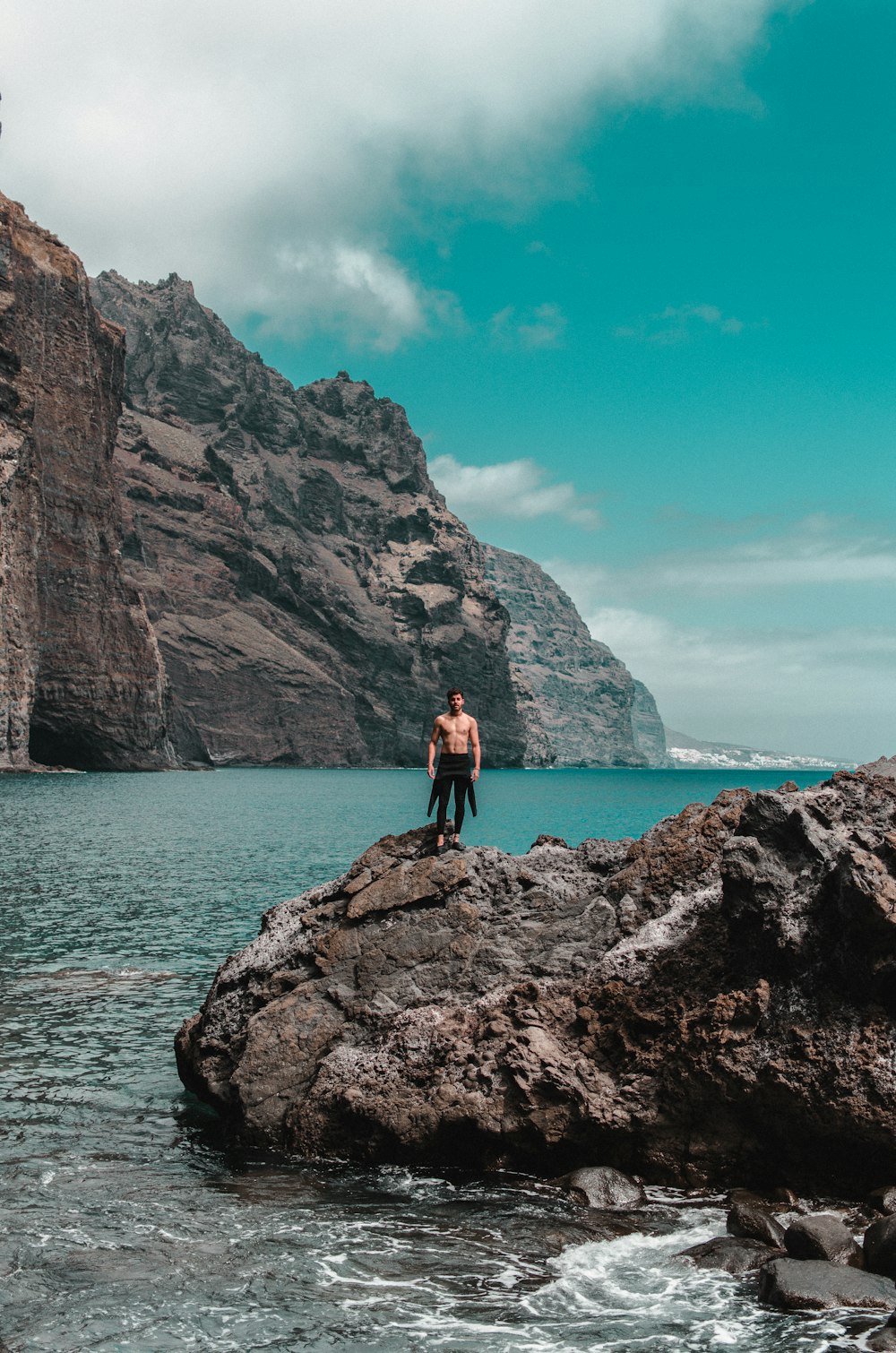 Oben-ohne-Mann, der tagsüber auf einer Felsformation in der Nähe des Ozeans steht