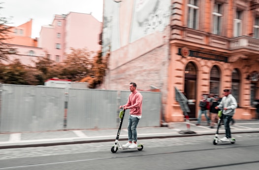 Two men riding kick scooters on a sunny day in Kampor, Rab