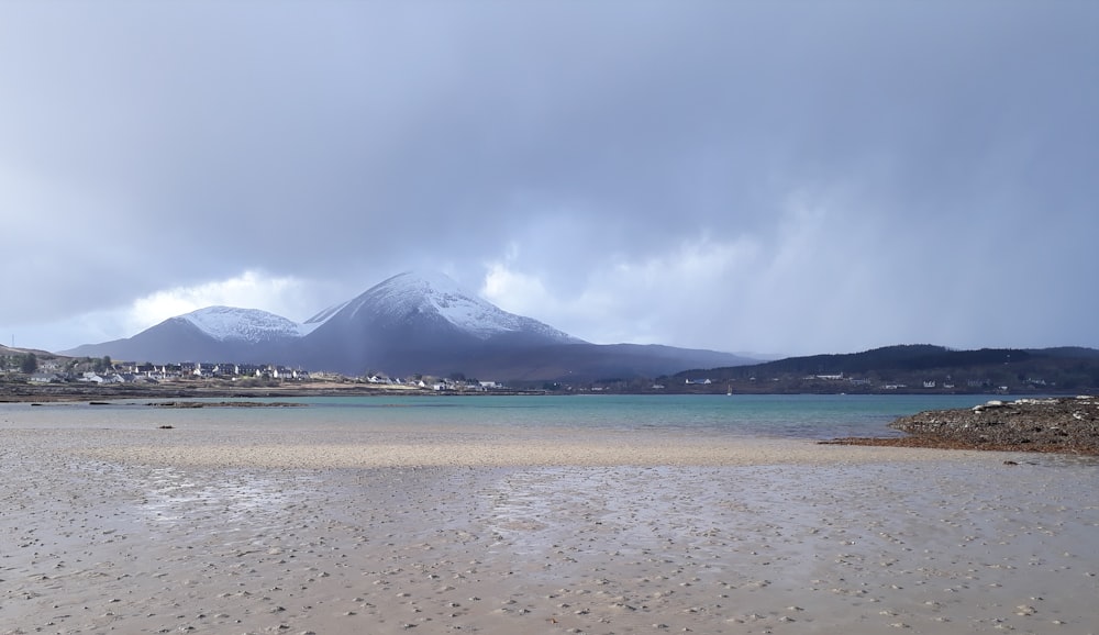 seashore with snow-covered mountain under grey clouds