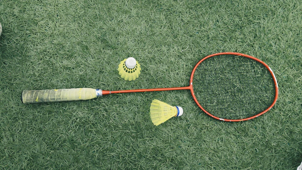 A close-up of two badminton rackets crossed on a wooden floor, highlighting different grip styles.