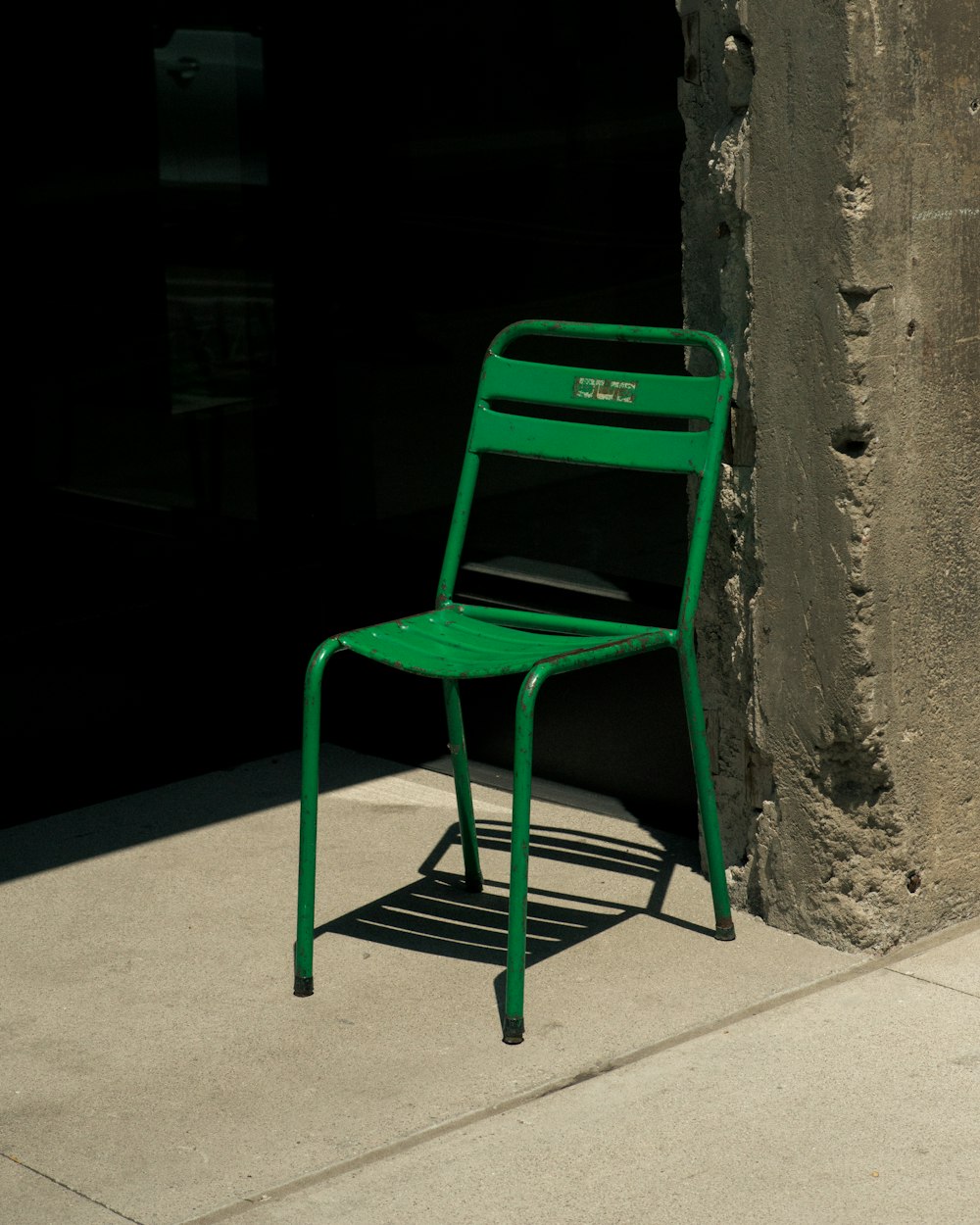 Grüner Stuhl ohne Armlehne aus Metall neben grauer Betonwand