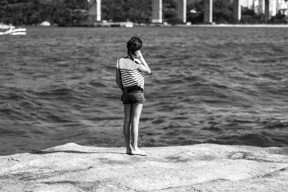 grayscale photography of girl standing near body of water