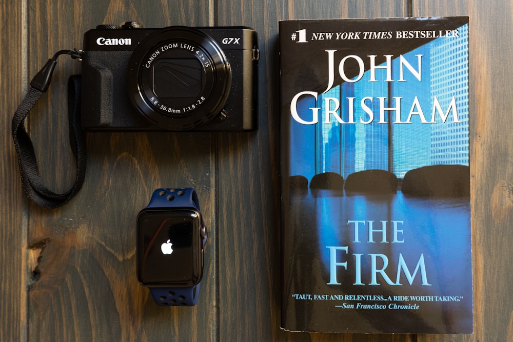 Fotocamera Canon G7X accanto a Apple Watch e al libro The Frim di John Grisham