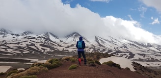 man standing on mountain with blue backpack during daytime