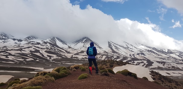 man standing on mountain with blue backpack during daytime