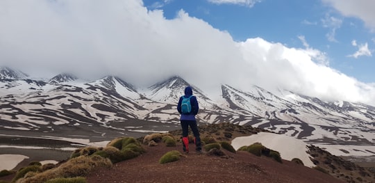 man standing on mountain with blue backpack during daytime in Ighil M'Goun Morocco