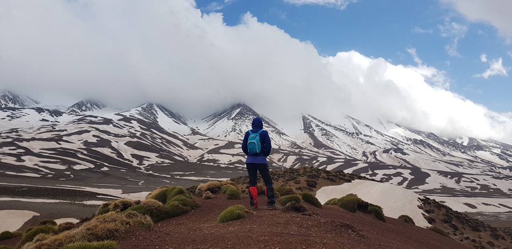 man standing on mountain with blue backpack during daytime